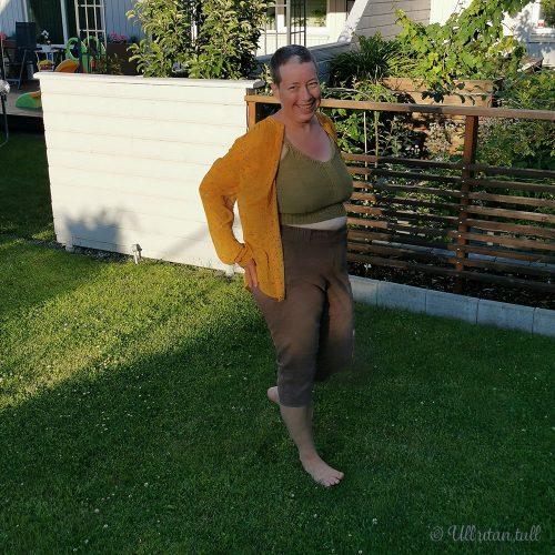 Marianne står på graset og har på seg strikka topp under ei oransje skjorte